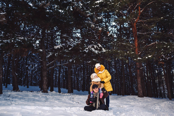 Feliz joven familia europea posando en el invierno sobre el telón de fondo de un bosque de pinos
 - Foto, imagen