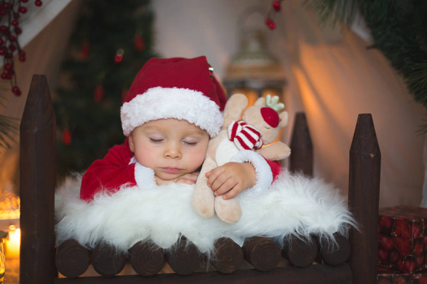 クリスマスの装飾クロース コスチューム、テントの前に赤ちゃんのベッドで寝ているカンタに身を包んだ愛らしい小さな幼児男の子 - 写真・画像