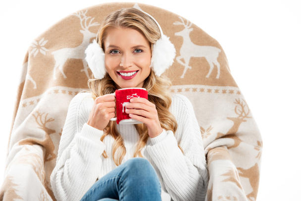 bella donna sorridente in possesso di tazza con bevanda calda e seduta in poltrona isolata su bianco
 - Foto, immagini