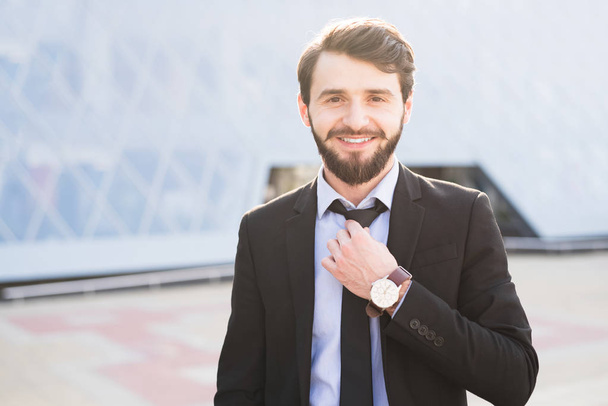 Muotokuva hymyilevä parrakas liikemies puvussa suoristaa solmionsa.
 - Valokuva, kuva