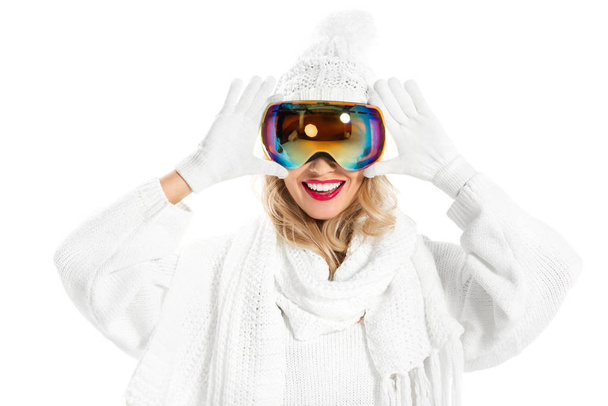 Cheerful woman in white knitted sweater, hat and mittens putting on ski goggles isolated on white - Photo, Image