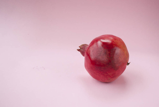 Ripe red pomegranate fruit on a pastel pink background with copyspace. Minimalistic style. - Foto, imagen
