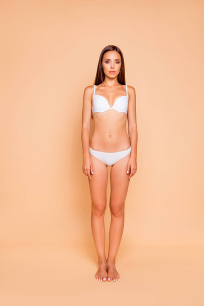 Full legs body size vertical portrait of gorgeous good-looking adorable brown-haired lady in her white underwear she stands isolated on pastel beige background look at camera - Foto, afbeelding