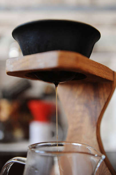 Making coffee in the black paperless porous ceramic porcelain filter on wooden coffee station. Devices for brewing in the background - Photo, Image