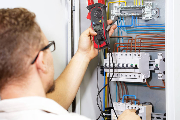 Electrician measures voltage with multimeter in electrical cabinet. An electrician is checking the voltage in an electric box. Adjustment of electrical control circuit for industrial equipment. - Foto, Imagem