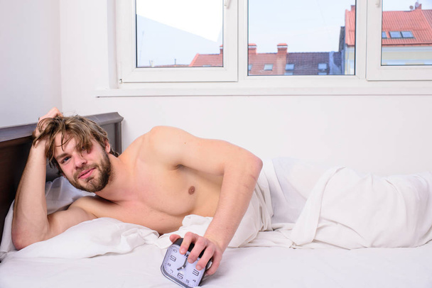 Good morning. Man unshaven lay bed hold alarm clock. Stick schedule same bedtime wake up time. Regulate your bodys clock. Enough sleep for him. Man unshaven tousled hair wakeful face having rest - Fotoğraf, Görsel