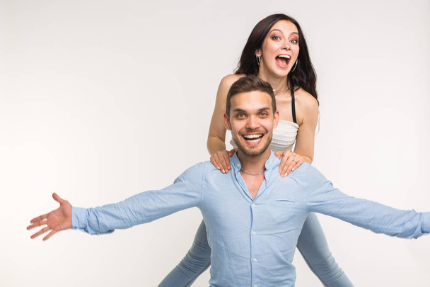 Onnellinen nuori tyttöystävä hyppää selkään poikaystävänsä valkoisella taustalla
 - Valokuva, kuva