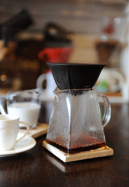 Kaffeezubereitung in schwarzem papierlosen porösen Keramik-Porzellanfilter auf einer Glasservierkanne. Tasse und Milchkanne mit Sahne - Foto, Bild