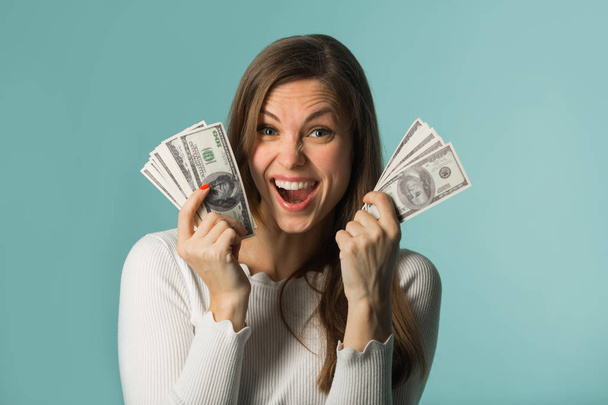 beautiful young girl with dollars in hands on a blue background - Foto, imagen