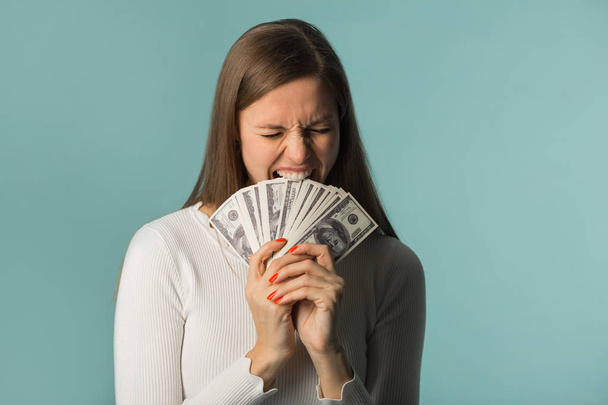 beautiful young girl biting teeth with dollars on a blue background - Foto, immagini