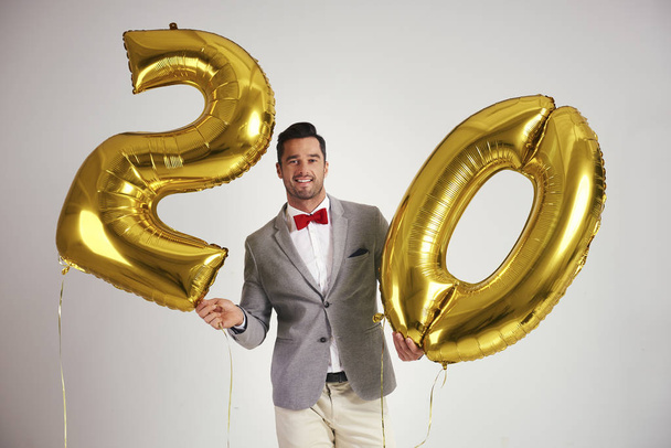 Молодой человек с золотыми шариками строит фигуру "20
" - Фото, изображение