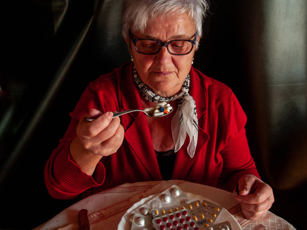 Koncepcja medycyny i opieki zdrowotnej. Senior kobieta z jej talerz pełen tabletki tabletki i pigułki jedzenie łyżką - Zdjęcie, obraz
