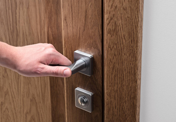 The man opens the door. Close - up of hand and door handle. Dark solid oak door - Foto, Bild