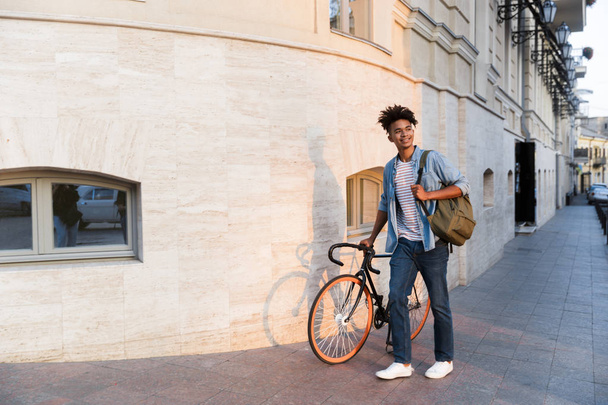 Image of happy young african guy walking with bicycle outdoors on the street. - Φωτογραφία, εικόνα