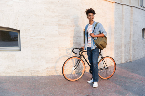 Photo of cheerful young african guy walking with bicycle outdoors on the street. - Valokuva, kuva