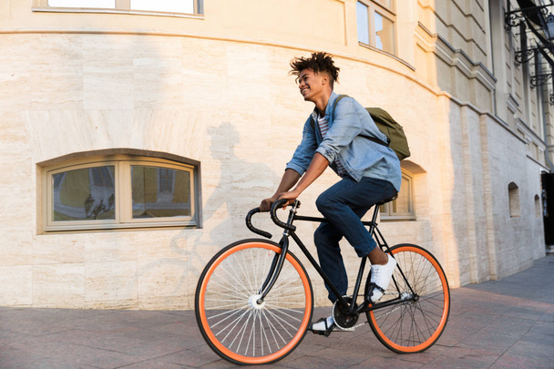 Photo of cheerful young african guy walking with bicycle outdoors on the street. - Valokuva, kuva