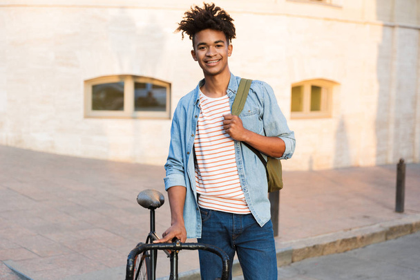 Photo of cheerful young african guy walking with bicycle outdoors on the street. - Foto, Imagem