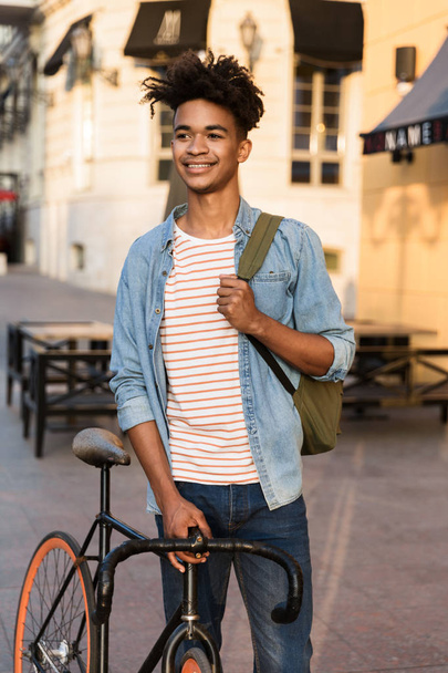 Image of happy young african guy walking with bicycle outdoors on the street. - Photo, Image