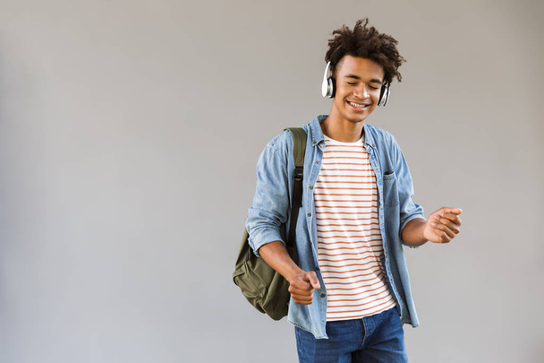 Image of cheerful young african guy standing outdoors listening music with headphones. - Foto, Imagen
