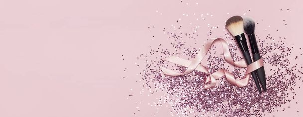 Дві різні косметичні пензлі з рожевою стрічкою та голографічним глютером у формі зірок на рожевому тлі Плоский копія простору зверху Макіяж аксесуари святкові новорічні
. - Фото, зображення