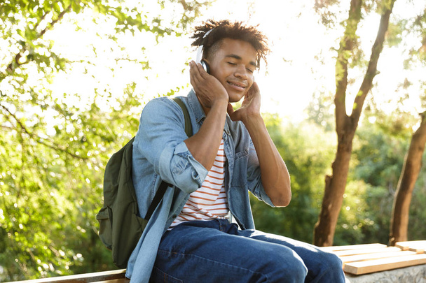 Image of handsome excited young african guy in park outdoors listening music with headphones. - Foto, imagen