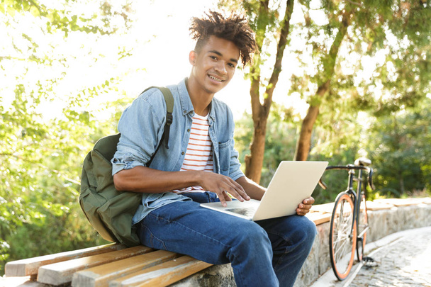 Image of handsome emotional young african guy in park outdoors using laptop computer. - Foto, Imagem