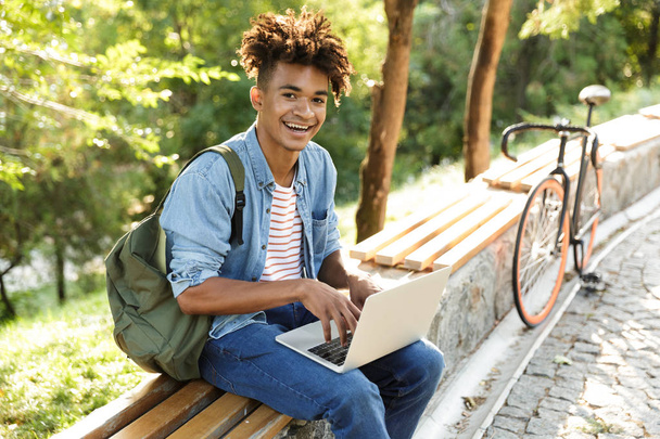 Image of handsome emotional young african guy in park outdoors using laptop computer. - Zdjęcie, obraz