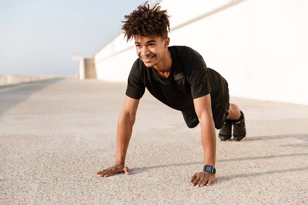 Strong young african man dressed in sportswear doing push-ups at the beach - Foto, Imagem