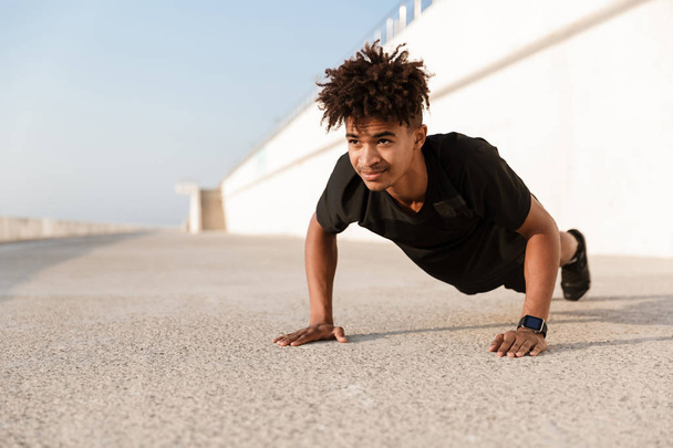 Confident young african man dressed in sportswear doing push-ups at the beach - Photo, image