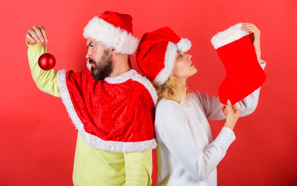 Woman and bearded man in santa hat waiting christmas red background. Couple christmas santa costume hold sock and ornament ball. Christmas stocking tradition. Christmas celebration concept - Photo, image