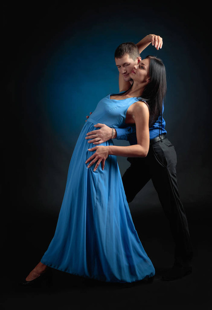 Young beautiful woman in long blue dress and man in blue shirt dancing tango. Couple in love dancing in the Studio. - Valokuva, kuva
