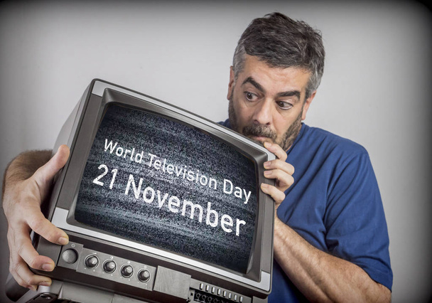 Μεσήλικας άνδρας κρατά μια τηλεόραση με παγκόσμια τηλεοπτική ημέρα 21 Νοεμβρίου οθόνη, εννοιολογική εικόνα - Φωτογραφία, εικόνα