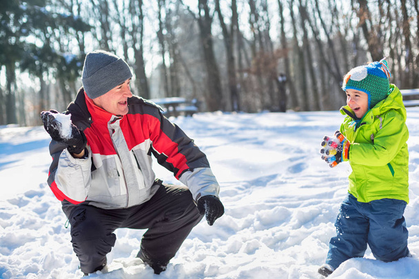 Grandfather throwing snowballs with his grandson on a bright sunny winter day - Foto, imagen