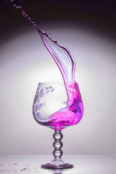 Transparent glass with a violet jet of liquid up, close-up - Фото, изображение