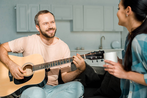 smiling husband playing acoustic guitar while wife listening - Fotó, kép