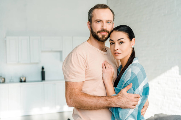 portrait of beautiful couple embracing and looking at camera at home - Photo, Image