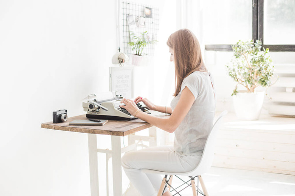 Young business woman working at home and typing on a typewriter. Creative Scandinavian style workspace - 写真・画像