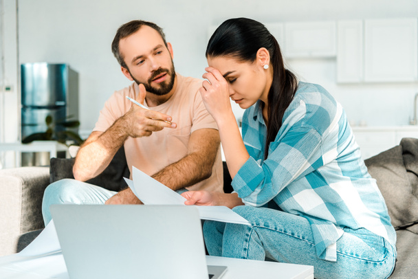 tired couple sitting on couch, using laptop and having financial problems at home - Photo, Image