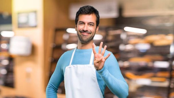 Człowiek na sobie fartuch szczęśliwy i liczenia cztery palcami w piekarni - Zdjęcie, obraz