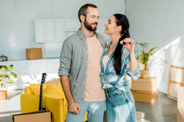 smiling couple embracing and holding keys from new house, moving concept - Photo, Image