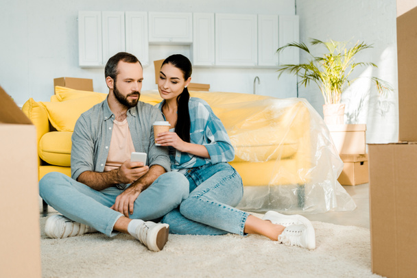beautiful couple drinking coffee, using smartphone and relaxing after packing for new house, moving concept - Foto, imagen