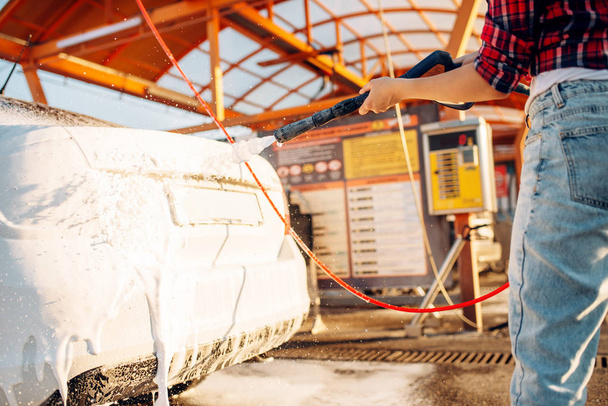 Mujer con pistola de agua de alta presión en las manos cubre el vehículo con espuma, lavado de coches sin contacto. Limpieza de vehículos al aire libre en verano
  - Foto, Imagen