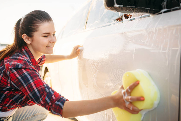 Young woman with sponge scrubbing vehicle with foam, car wash. Lady on self-service automobile washing. Outdoor carwash - Photo, Image