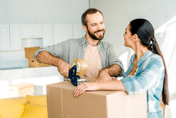 husband and wife packing cardboard box with scotch tape, moving concept - Photo, Image