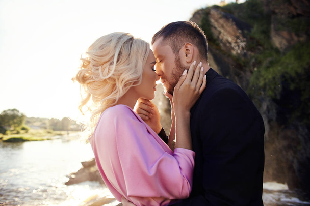 Portrait of a couple in love close-up on a beautiful Sunny day at sunset. Love emotions and hugs in the sun. Blonde woman and man with beard look at each other - 写真・画像