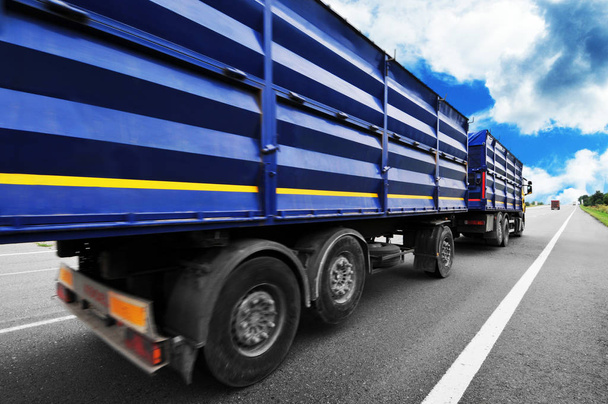 Achteraanzicht van grote vrachtwagen met blauwe trailers op platteland weg tegen blauwe hemel met wolken - Foto, afbeelding
