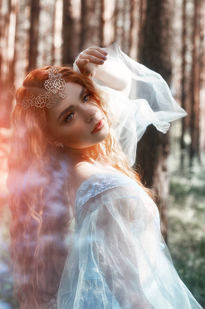 Beautiful redhead woman forest nymph in a blue transparent light dress in the woods spinning in dance. Red hair girls. Art fashion portrait of fairy woman fairy tale in summer forest - Фото, зображення