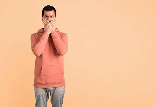 Um homem com uma camisola cor-de-rosa a cobrir a boca com as duas mãos por dizer algo inapropriado. Não pode falar em fundo ocre
 - Foto, Imagem