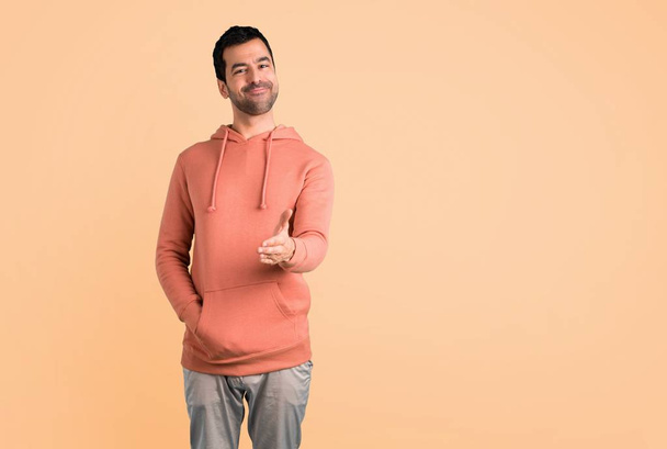 Man in a pink sweatshirt shaking hands for closing a good deal on ocher background - Photo, Image