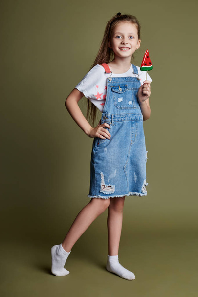 Beautiful young smiling teen girl holding a Lollipop in the form of a slice of watermelon. Cheerful joyful emotions on the girl face - 写真・画像
